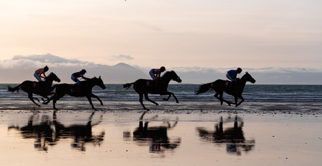 Silhouettes of race horses and jockeys racing on the beach, wild Atlantic way on the west coast of...