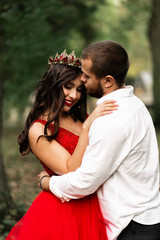 Fototapeta premium Beautiful romantic couple kiss closeup. Attractive young woman in red dress and crown with handsome man in white shirt are in love. Happy Saint Valentine's Day. Pregnant and wedding concept.