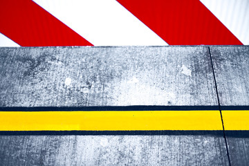Abstract detail of road signage, red and white direction indicators and bright yellow reflective band painted on rough gray concrete pavement.