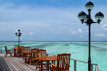 wooden cafe tables and chairs on a tropical island sea, with a beautiful view of turquoise shallow...