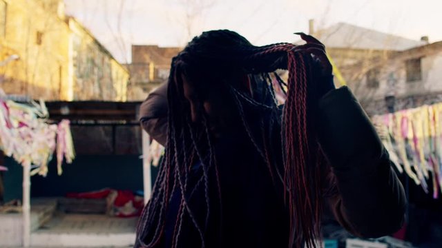Young woman spinning with colorful dreadlocks. Stock footage. Stylish woman with dreadlocks turns to show them off. Beautiful woman with dreadlocks at theme festival