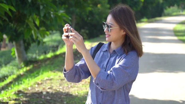 4k Young beautiful happy Asian woman walking through tea plantation and using smartphone taking a photo of nature in spring summer. Cheerful Asian woman relaxing and enjoying outdoor life in nature.
