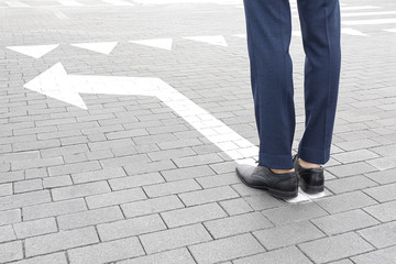Young businessman standing on road with arrow marking. Concept of choice