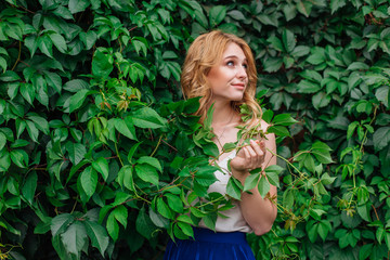 Portrait of a young beautiful woman, standing next to the wall of wild grape leaves.