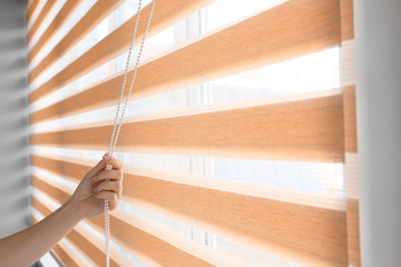 Woman opening blinds on window - obrazy, fototapety, plakaty