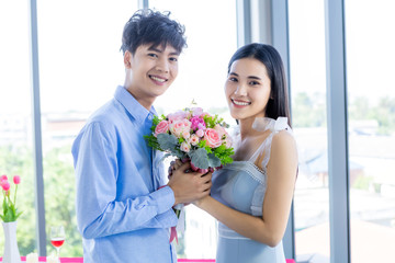 Valentine's day concept,asian Young happy sweet couple holding bouquet of red and pink roses After lunch In a restaurant background