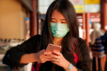 young beautiful Asian Chinese student woman at airport wearing protective facial mask checking news and information with mobile phone on China Coronavirus epidemic outbreak