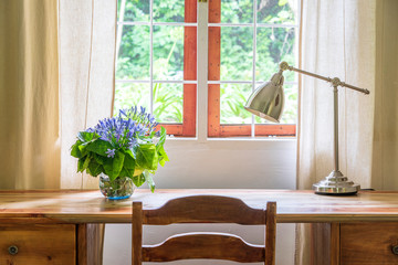 Wooden table with chair, lamp and a bouquet of flowers near the window in modern working area at...