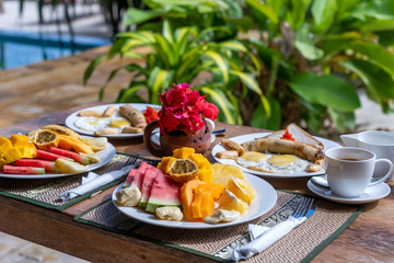 Tropical breakfast of fruit, coffee and scrambled eggs and banana pancake for two on the beach near sea