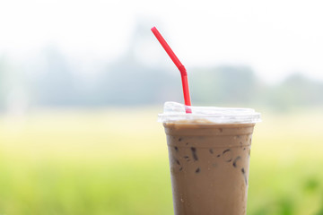 Close up glass of ice cappuccino coffee on wood table with green nature background, selective focus