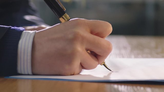 closeup of hand holding pen and signing on document