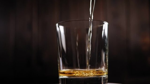 Close-up of whiskey poured into an empty glass that rotates around itself on a black background. Slow motion. Artificial lighting. The concept of expensive alcoholic beverages.