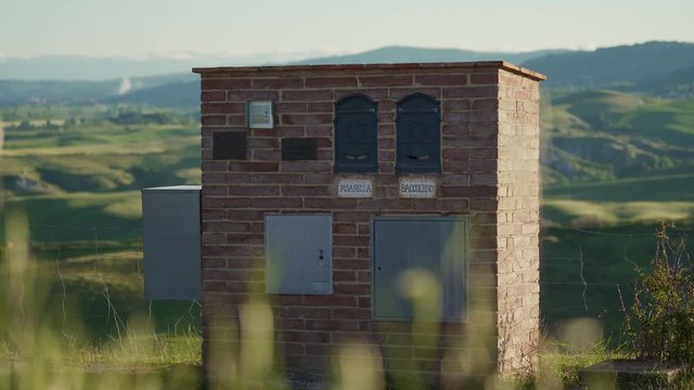 Brick building with mailboxes for two families on background of green hills