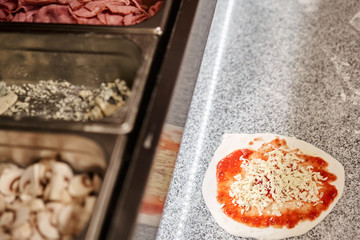 Cooking pizza. arranges cheese ingredients on the dough preform. Closeup hand of chef baker in uniform white apron cook at kitchen