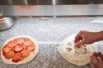 Cooking pizza. Lays out mushrooms and cream sauce, ingredients on the dough preform. Closeup hand of chef baker in uniform white apron cook at kitchen