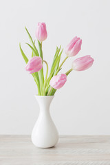 pink tulips in white ceramic vase on wooden table on background white wall