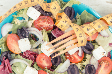 Tape measure with fresh greek salad with feta cheese and vegetables. Best food for dieting and...