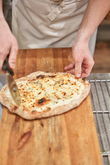Italian kitchen and cooking concept. Chief with a pizza cutter cutting pizza to pieces at Neapolitan pizzeria.