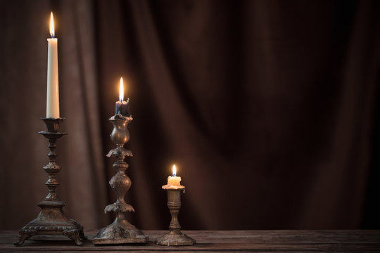 antique candlestick with burning candle on old wooden table on background brown velvet curtain