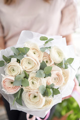 Persian buttercup in womans hands. Bunch pale pink ranunculus flowers with green eucalyptus. The work of the florist at a flower shop