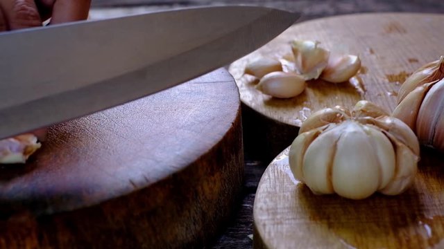 Close-up knife cutting garlics for cooking on wooden board, old style kitchen