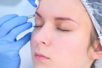 Cosmetologist plucks out hair on eyebrows with tweezers for woman, face closeup. Eyebrows tweezing procedure. Beautician is making brows correction with cosmetic tweezer. Beauty industry.