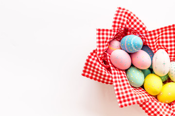 Easter eggs painted in basket on white desk top-down copy space