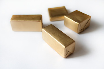 Chocolate candies wrapped in golden foil isolated on white surface. Template for greeting card, poster or invitation. Sweets scattered on white smooth table. Backdrop or background