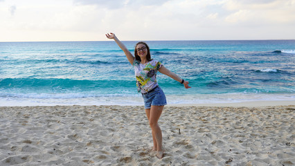 young girl in denim shorts on a sandy beach near the ocean. brunette walks on a background of blue clear water of the Pacific Ocean.