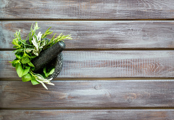 Herbs in ceramic mortar with pestle on dark wooden backgroud top-down copy space