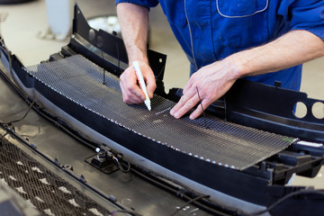 Hands of a professional mechanic at work. Trimming the mesh from stones falling into the front bumper of the car. Car tuning in a car service.