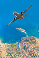 Obraz premium White passenger jet plane in the sky - Aircraft flies high over the city and sea coast of Kusadasi port and island - Kusadasi, Izmir