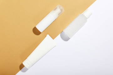 Facial and body care cosmetics bottles composition on brown background. Gel tube, lotion, micellar water and unbranded blank packages. Skincare female products advertising with white backdrop flat lay