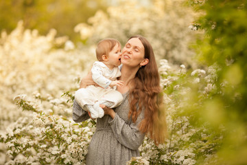 Beautiful young, happy woman with a baby in the spring in a blooming garden, smiling. Concept: spring. Happiness. Mother's day. Relationships in the family. March 8.