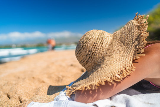 Beach suntan woman sleeping hiding under straw hat covering from sun lying down sunbathing on Caribbean travel vacation. Girl sleeping in shade.