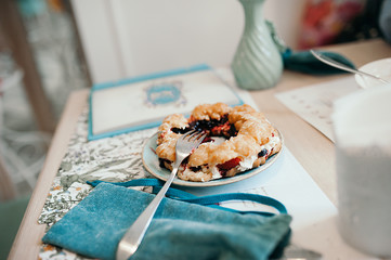 a piece of cake with berries on a plate with a fork is on a white table and a turquoise napkin, morning breakfast in a cafe, table setting in turquoise color