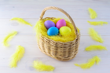 Easter eggs in a basket with feathers on a wooden table.