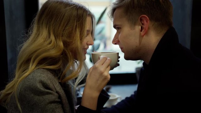 couple on a date in cozy cafe, talking, drinking coffee from one cup and having fun together. people sitting at cafe window, Valentines day concept