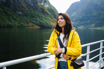 The girl tourist on a pleasure boat on the fjord enjoys the picturesque mountains and lakes of Norway. Young woman posing against the backdrop of the mountains. Travelling, lifestyle, adventure.