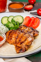 Grilled chicken thighs with fresh vegetables on a white plate