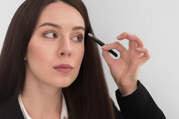girl with make-up with long dark hair in a business suit corrects his eyebrow tweezers, on a white background