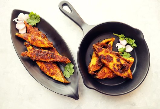 Marinated Pomfret fried fish or Indian Spicy fish fry garnished with onion and coriander on iron skillet griddle, selective focus with copy space.