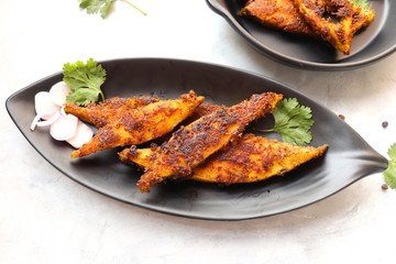 Marinated Pomfret fried fish or Indian Spicy fish fry garnished with onion and coriander on iron skillet griddle, selective focus with copy space.