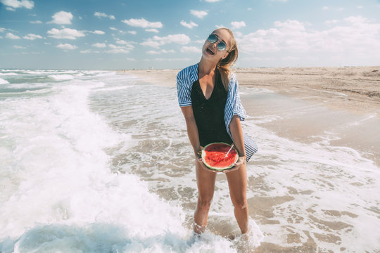 Slim girl in fashion swimwear eating watermelon at sand beach by sea