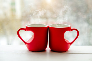 two heart shaped mugs with tea on the background of a window in winter