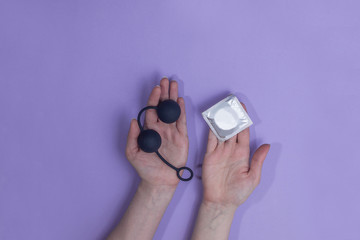  Anal balls and condoms in hands, on a colored background. top view. Sex toy, comfortable sex,...