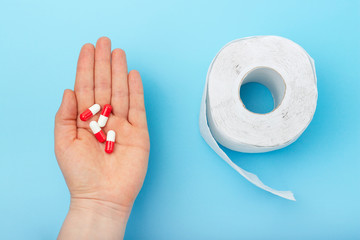 Female hand with pills and roll of toilet paper on blue background, a concept of diarrhea or...