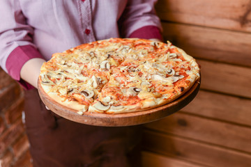 Waiter holds a plate of tasty food. Italian cuisine in restaurant. Delicious pizza with chicken meat, mushrooms, sause.