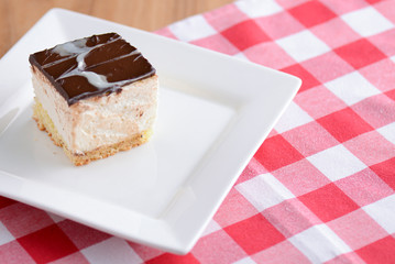 Fototapeta na wymiar Chocolate souffle with thick chocolate ganache glaze served on a white plate on red plaid background