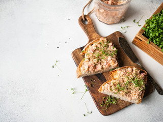Healthy toasts with salmon pate and fresh green sprouts on yeast-free bread on wood cutting board on grey background. Copy space - obrazy, fototapety, plakaty